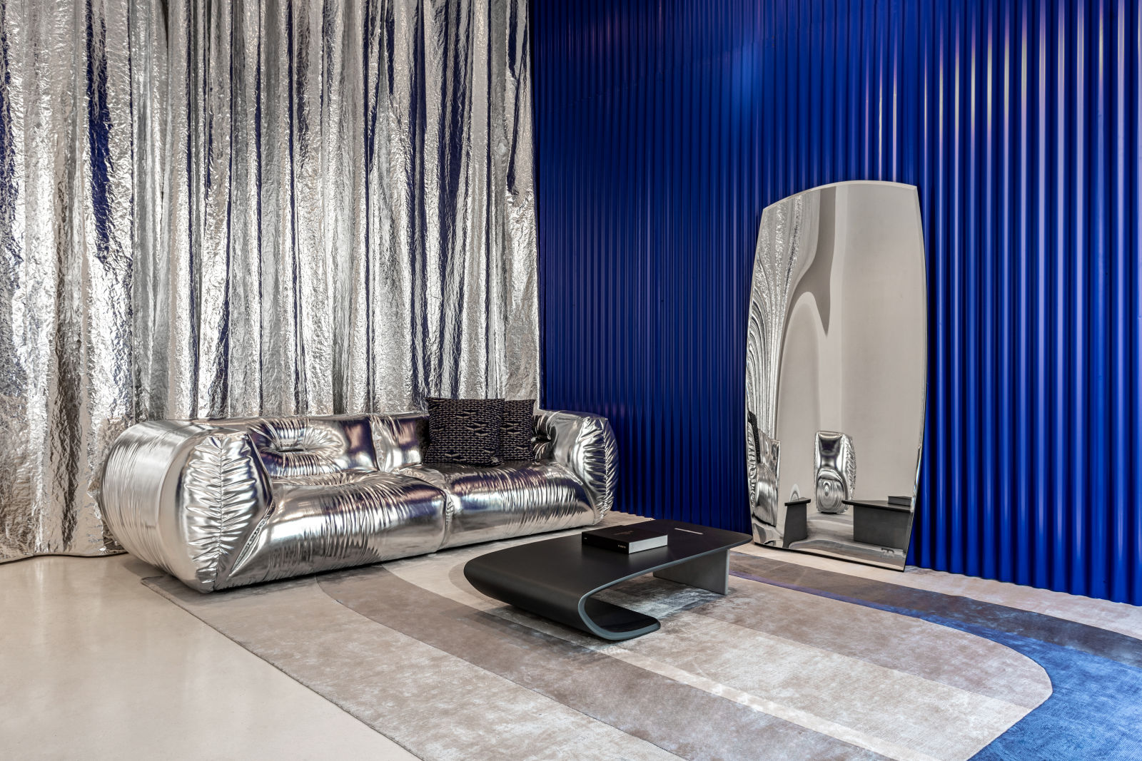 A striking interior featuring a sleek, metallic sofa and a contemporary coffee table, set against bold blue and shimmering silver walls, embodying the luxurious and innovative style of Bugatti Home.