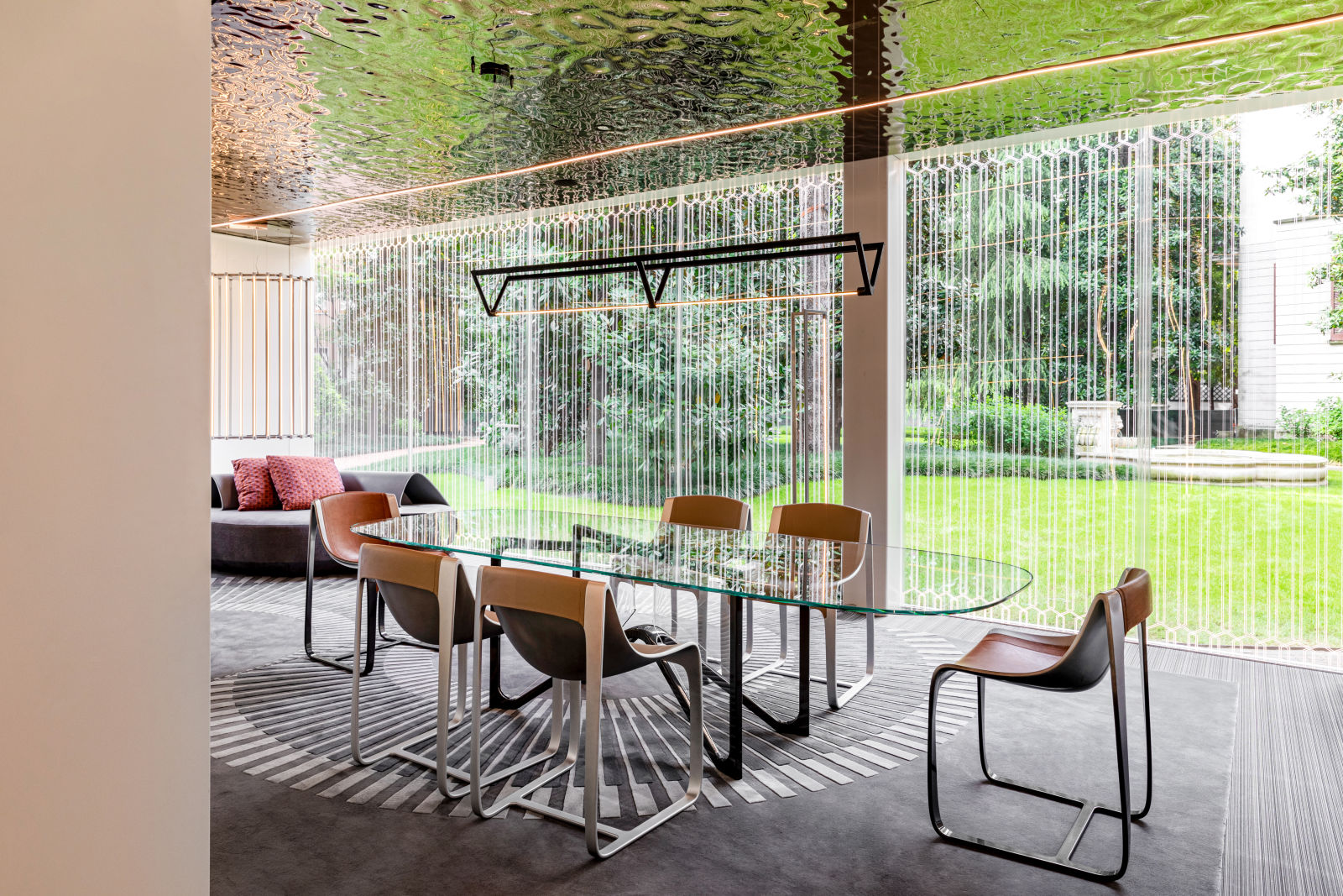 A modern dining area featuring a glass table surrounded by stylish chairs, complemented by a unique textured ceiling and a view of a lush garden, all reflecting the luxurious and innovative design of Bugatti Home.