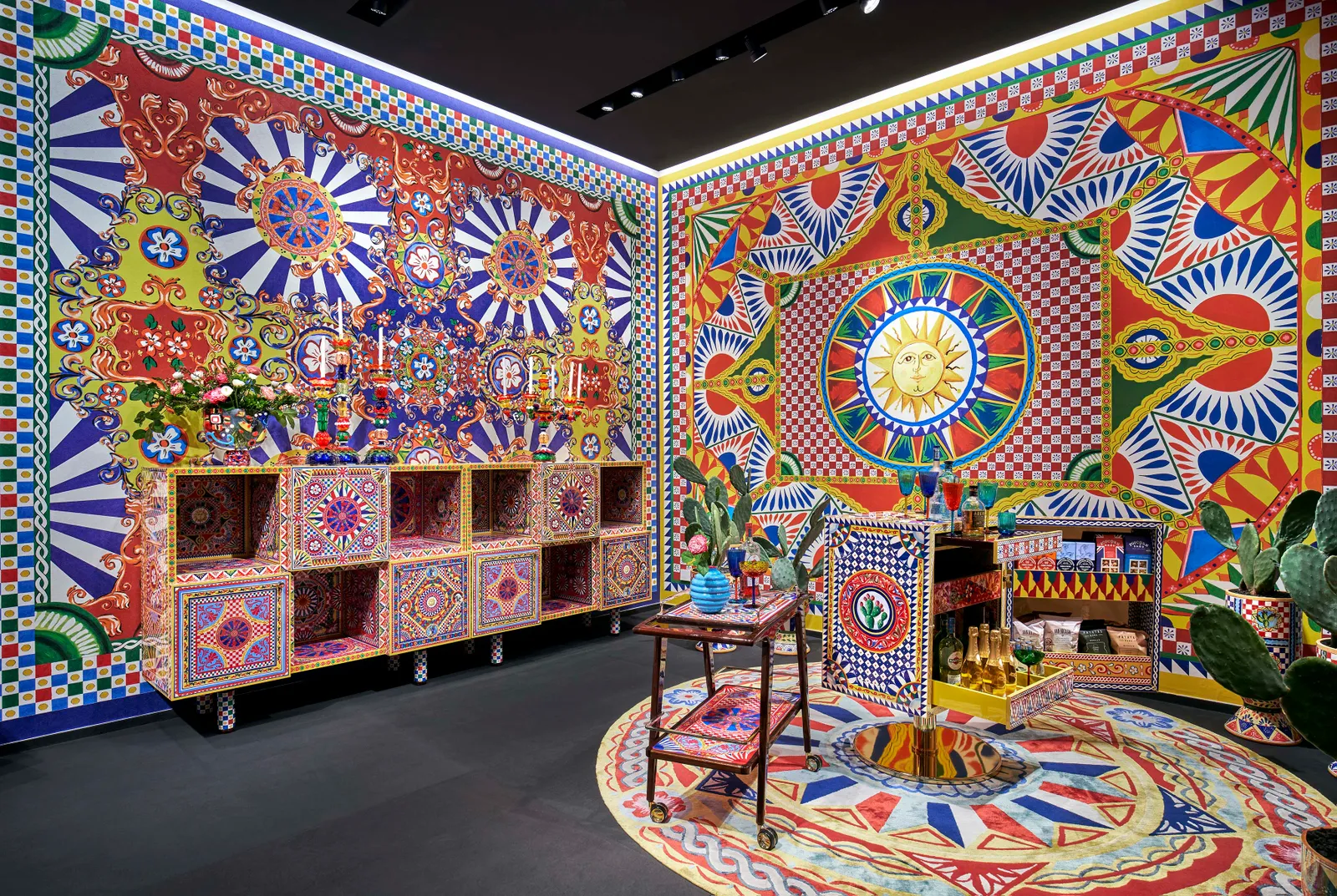 A vibrant interior featuring Dolce & Gabbana Casa's Carretto print, showcasing decorative cabinets and a serving cart against bold patterns.