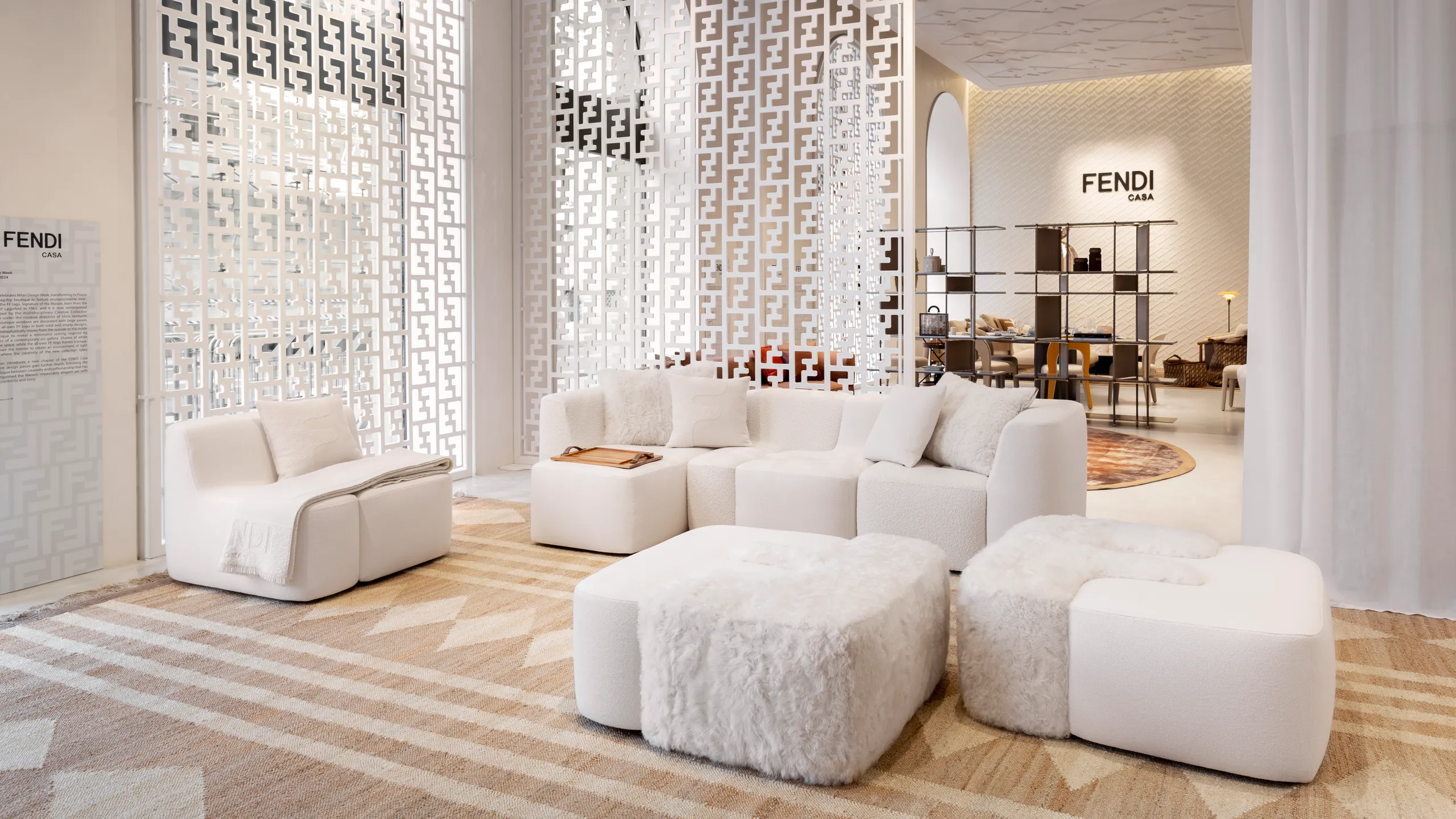 A stylish living area featuring Fendi Casa furniture, including a plush white sectional sofa and textured ottomans, complemented by an intricate partition and a warm rug.