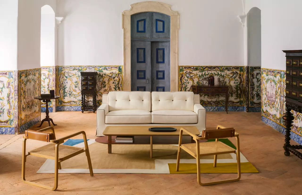 A stylish living area by Hermès featuring a cream sofa, modern chairs, and an elegant coffee table, set against ornate wall decor and a blue door.