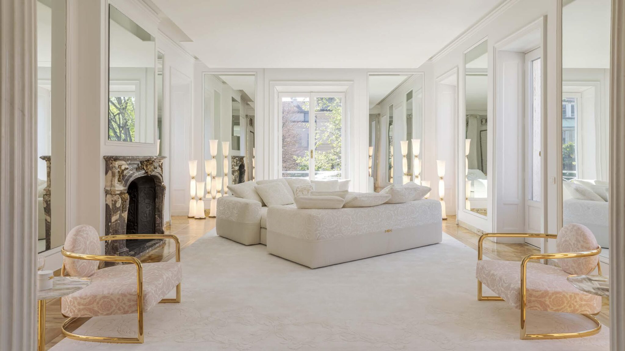 A luxurious living space featuring elegant Versace furnishings, including a plush white sofa and stylish armchairs, complemented by sophisticated mirrors and ambient lighting.