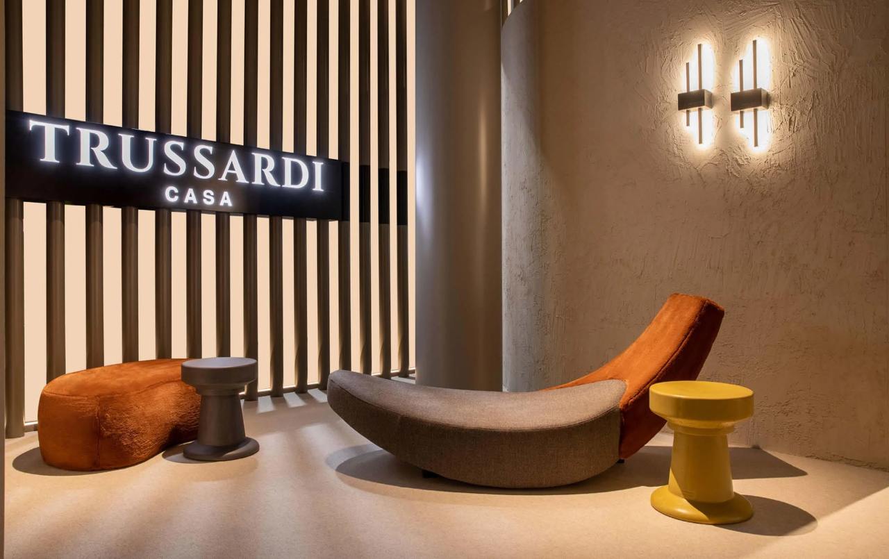 A stylish seating area by Trussardi Casa featuring a curved lounge chair in gray and orange, complemented by colorful side tables.