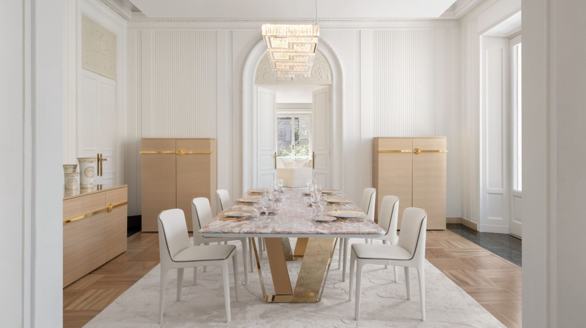 An elegant dining space featuring a luxurious marble table and chic white chairs, complemented by Versace furnishings and exquisite lighting, creating a sophisticated atmosphere.